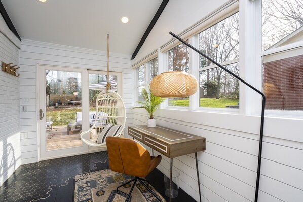 A modern interior with a wooden desk, a hanging rattan light fixture, and a view of the outdoors. - Boho-Chic South CLT Oasis ★ Custom Home ★ Sleeps 6 (Charlotte)