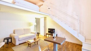 A modern living room with a sofa, a coffee table, a TV, and a dining area with a table and chairs. A staircase is visible in the background. - LUXURY UFFIZI - Three Bedroom Apartment, Sleeps 12 (Florence)