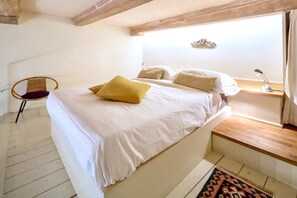 Un dormitorio con una cama, una silla, una mesita de noche y una ventana.
