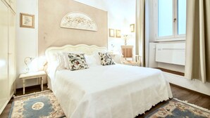 Une chambre avec un grand lit, une table de chevet, une lampe fixée au mur et une fenêtre avec des rideaux.