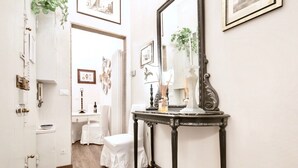 Un couloir étroit avec une porte blanche, une petite table surmontée d’un miroir et une chaise blanche.