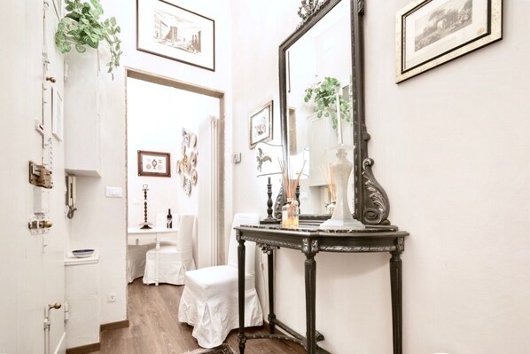 A narrow hallway with a white door, a small table with a mirror, and a white chair.