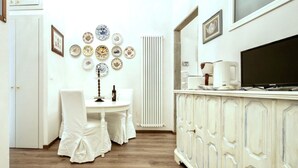 Un coin repas avec une table et des chaises blanches, un radiateur et un meuble contenant un téléviseur.