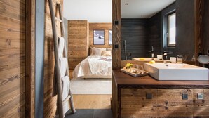 Un dormitorio moderno con una pared de madera, una cama con ropa de cama blanca, una mesita de noche con una bandeja y un espejo grande sobre el lavabo.