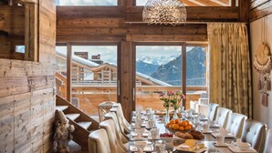 Un comedor con una mesa de vidrio preparada para el desayuno, paredes de madera y vistas a la montaña.