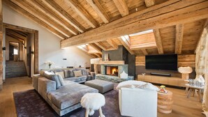Un loft amplio con vigas de madera a la vista, una chimenea, un televisor de pantalla plana grande y una zona de estar acogedora con un sofá mullido y un reposapiés.