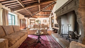 Un salón tradicional con techo de madera, chimenea y alfombra roja estampada.