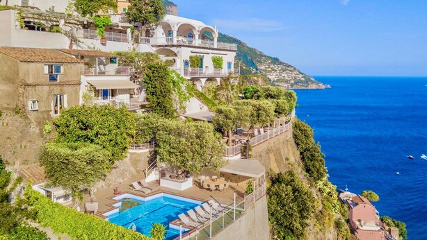 A coastal hotel with a swimming pool, outdoor seating, and a view of the sea.