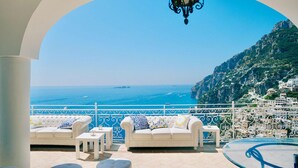 A balcony with white furniture, a view of the sea, and a mountainous landscape.