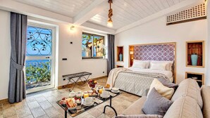 A hotel room with a bed, a sofa, a dining table with breakfast, a window with a view, and a ceiling fan.