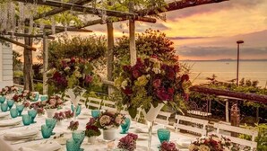 Un espace extérieur aménagé pour les repas, avec des tables blanches, de la vaisselle bleue et des centres de table floraux.