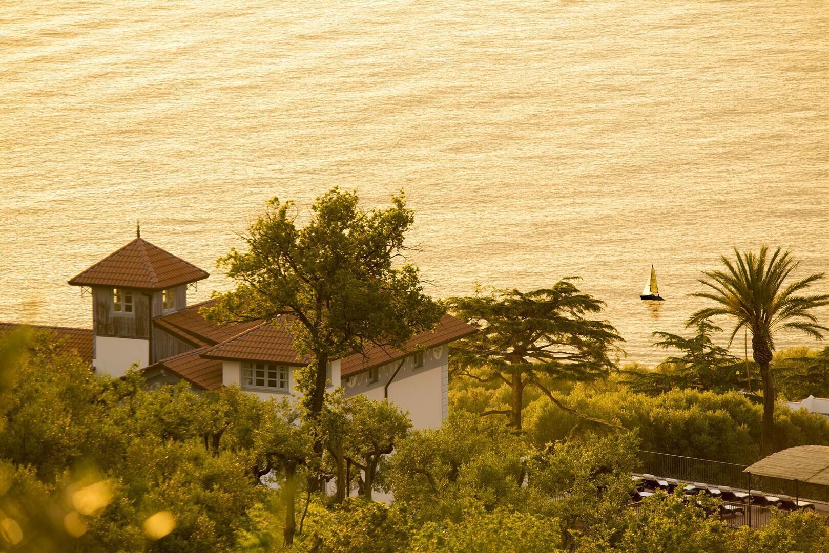 Un bâtiment situé sur la côte, doté d’une tour, entouré d’une végétation luxuriante et offrant une vue sur la mer.