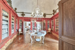 A library with red walls, bookshelves, a chandelier, and a round table with books. - VILLA GRANDUCA - Six Bedroom Villa, Sleeps 12 (Pistoia)