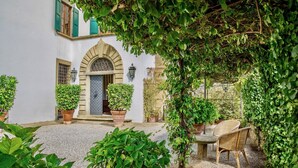 Une cour avec un bâtiment blanc, un espace de repos abrité et des plantes en pot.