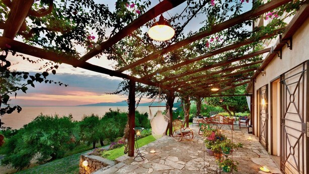 A covered patio with stone flooring, wicker furniture, and hanging chairs overlooking a body of water. - VILLA MARATEA - Six Bedroom Villa, Sleeps 12 (Maratea)