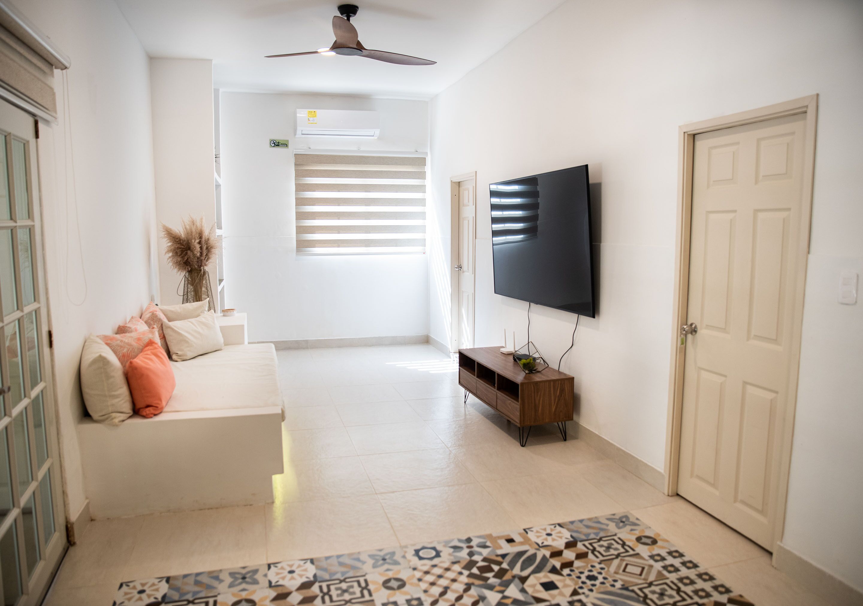 Un salon moderne avec un téléviseur à écran plat, un canapé, un tapis à motifs et un ventilateur de plafond.