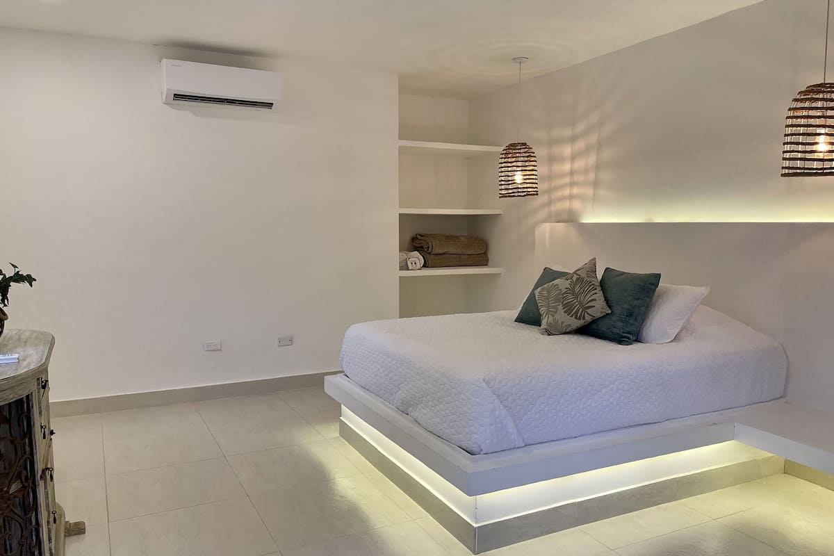 A modern bedroom with a bed, built-in shelves, an air conditioning unit, and pendant lights.