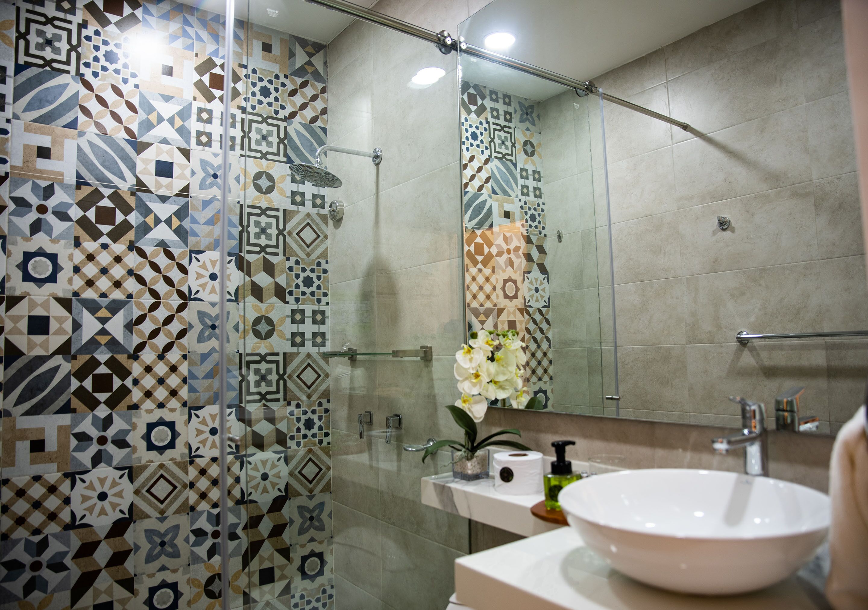 A bathroom with patterned tiles, a glass shower enclosure, a sink with a mirror, and a toilet.