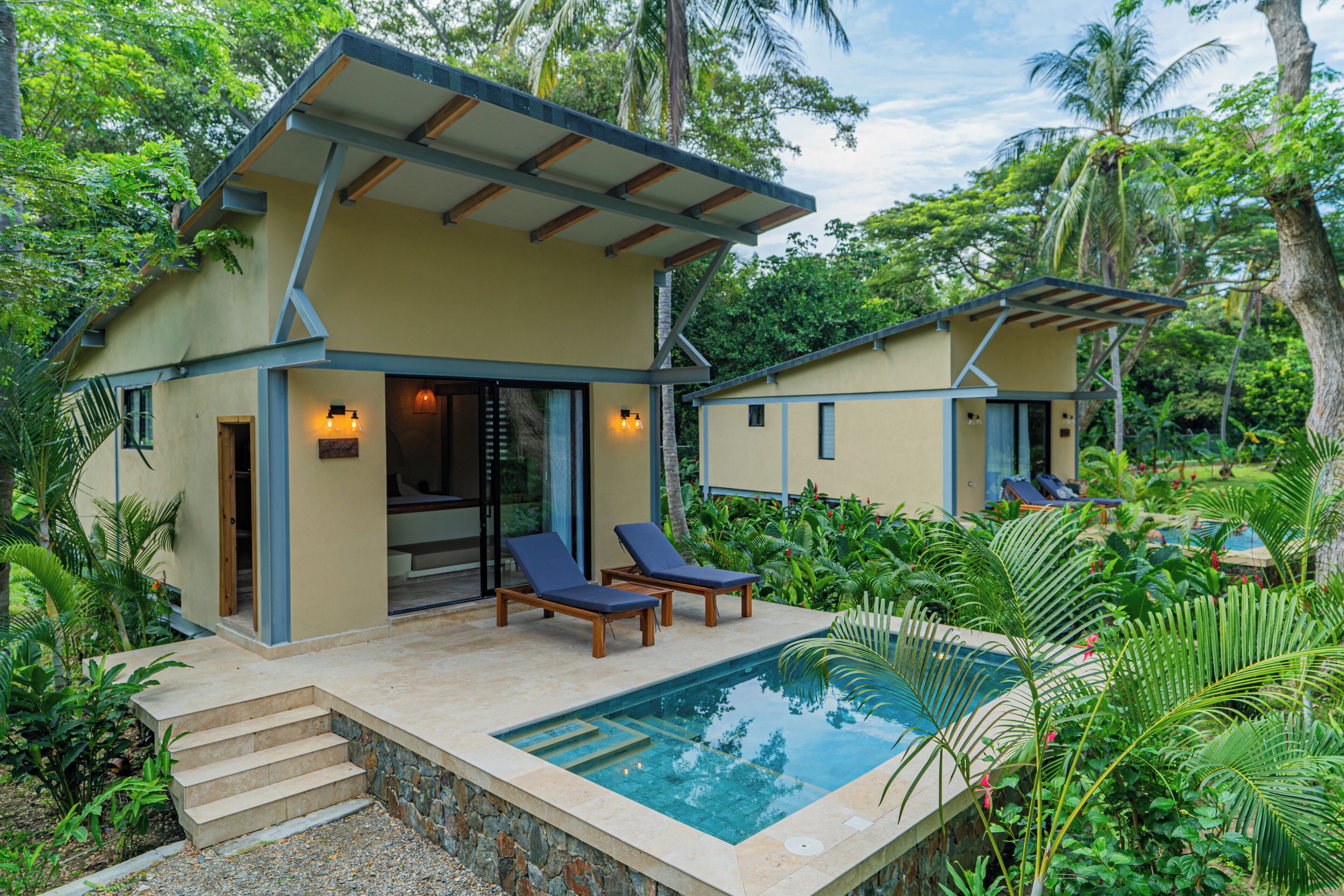Une maison à deux étages avec une piscine, une terrasse en bois et des chaises longues.