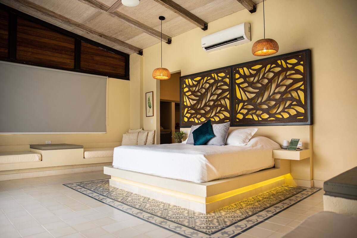 A modern bedroom with a large bed, a decorative headboard, a small bedside table, and a wall-mounted air conditioner.
