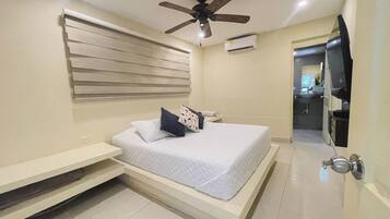 A bedroom with a bed, a ceiling fan, an air conditioning unit, and a view of the bathroom.