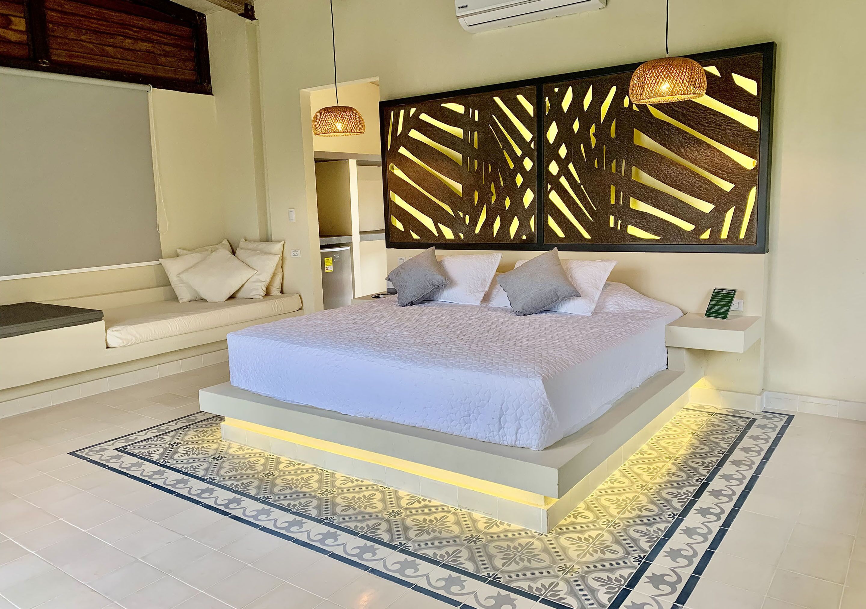 Un dormitorio moderno con una cama grande, un sofá, un panel decorativo en la pared y una lámpara colgante.