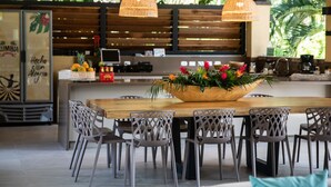 Restaurante com mesa e cadeiras de madeira, um grande arranjo de flores e luminárias pendentes.