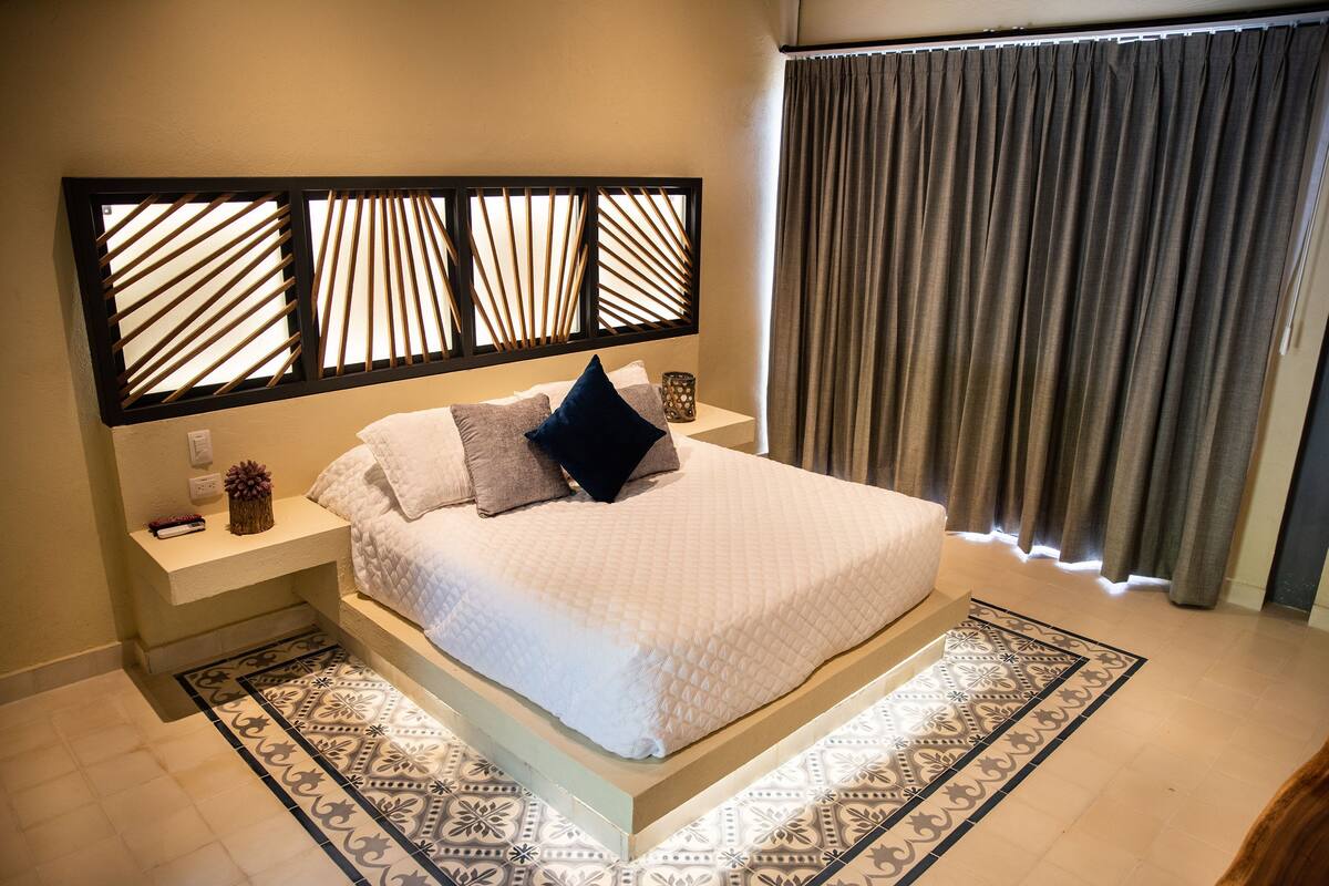 A modern bedroom with a large bed, a nightstand, a decorative headboard, and a patterned rug.