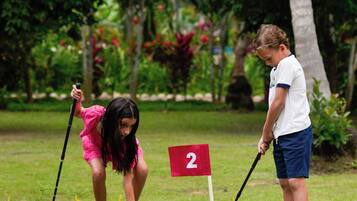Campo de golf con una bandera roja marcada con el número 2 y una zona de práctica de putts con rocas y césped.