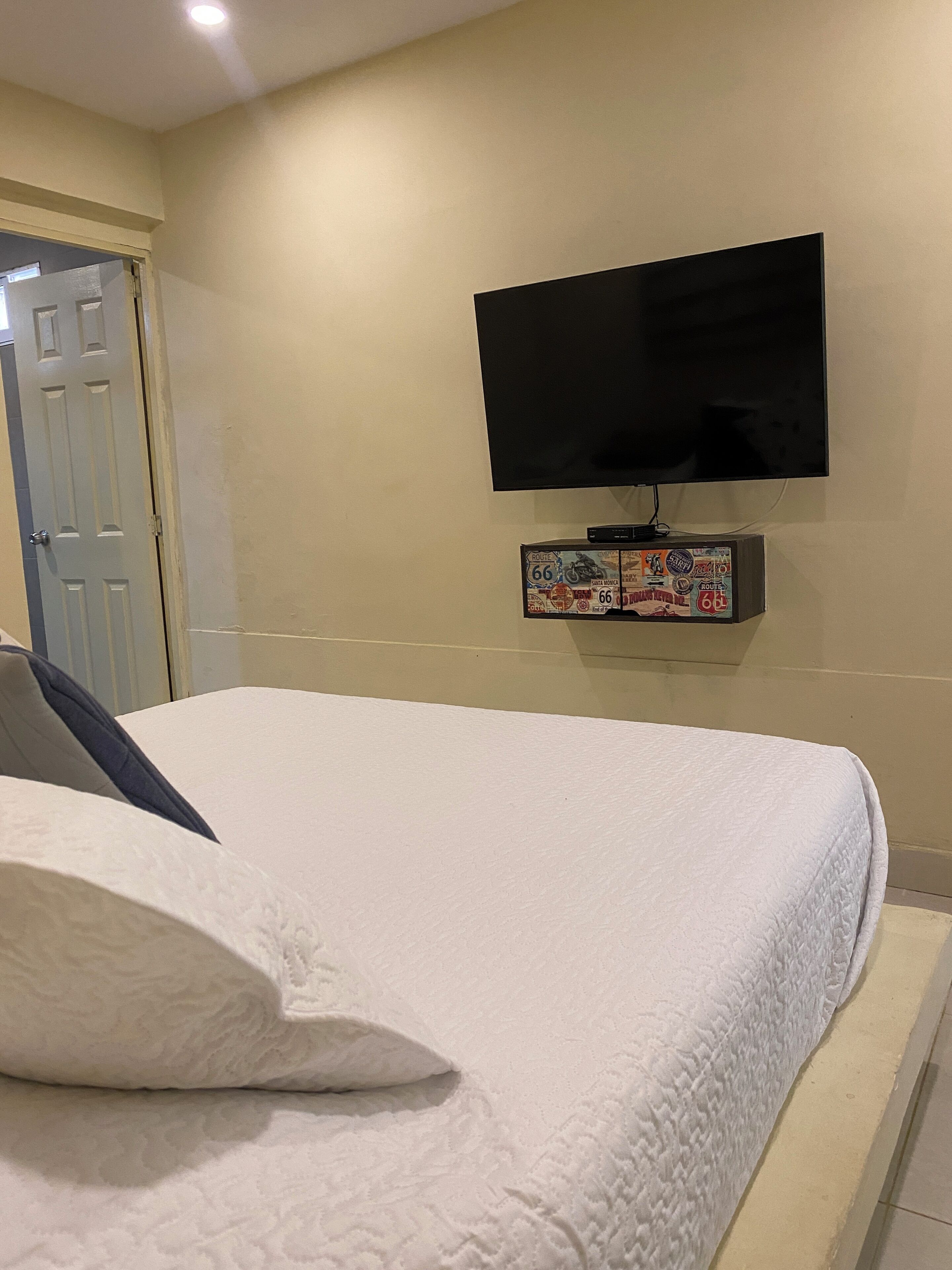 Une chambre à coucher avec un lit, un téléviseur fixé au mur et une porte.