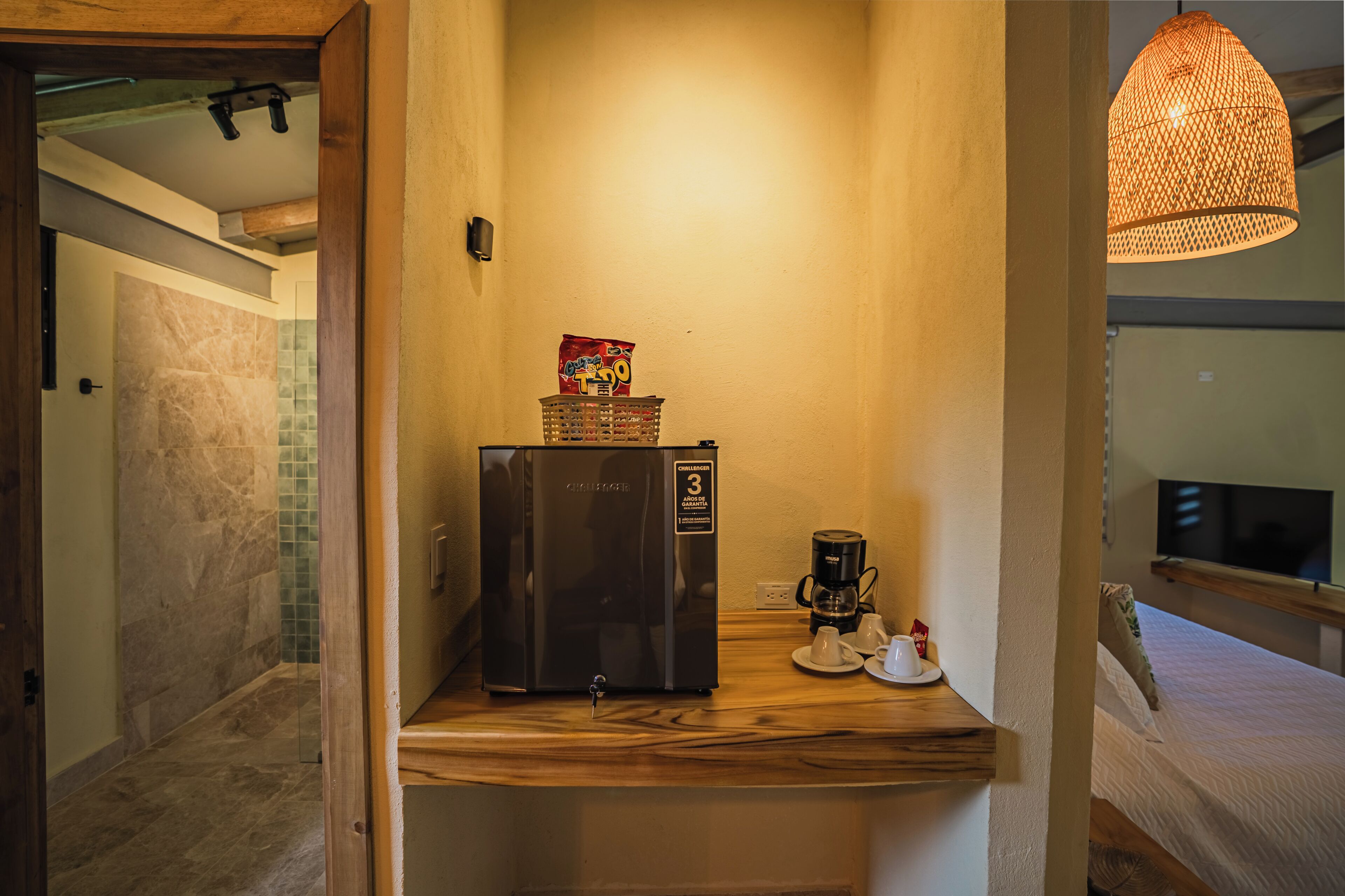 Une petite cuisine équipée d’un réfrigérateur, d’une machine à café et d’un luminaire suspendu.