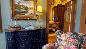 Une pièce avec un buffet en bois foncé, un fauteuil à motifs floraux, un tableau et une lampe.