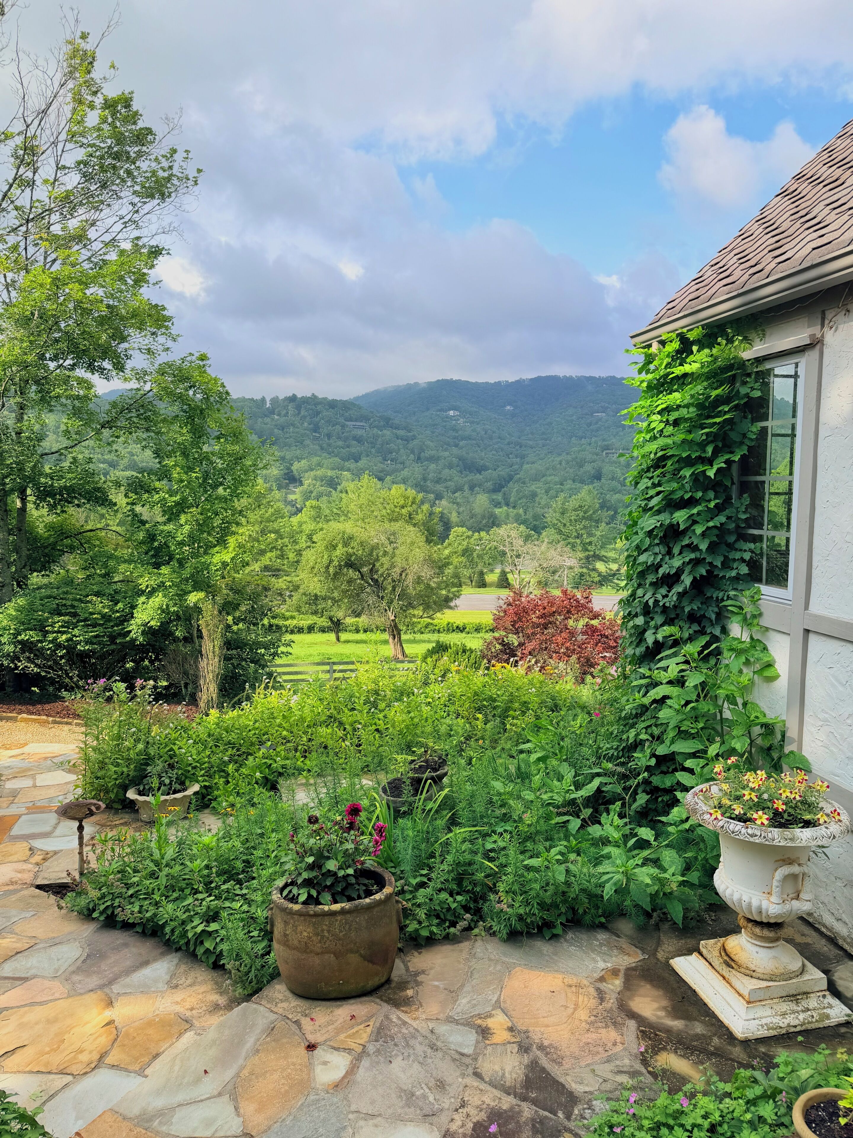 Un jardin avec un sentier de pierres menant à une maison qui offre une vue sur une vallée verdoyante.