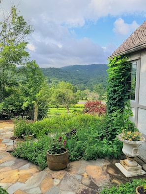 A garden with a stone pathway leading to a house with a view of a lush valley. - Elegant Tudor Cottage: Farm Animals, Views, Vintage Decor (Banner Elk)
