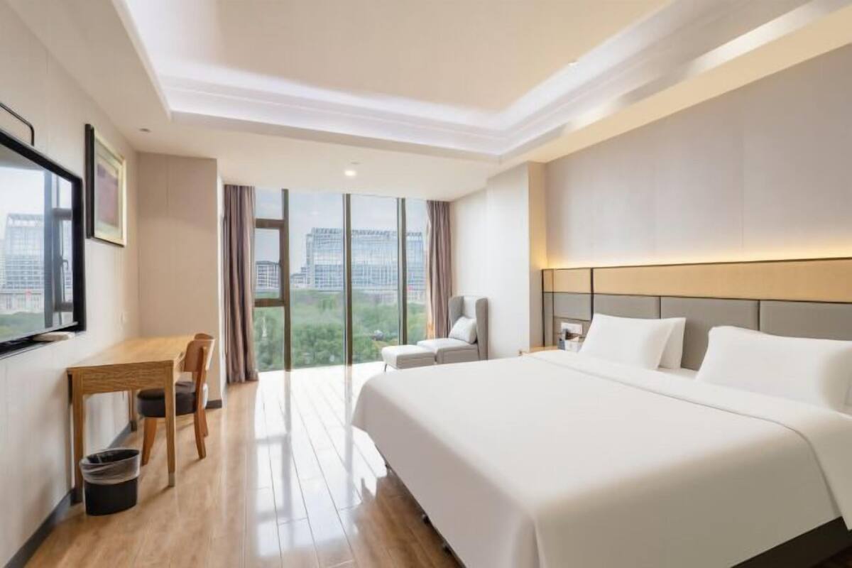 Quarto de hotel com uma cama grande, uma escrivaninha, uma cadeira e vista para a cidade.