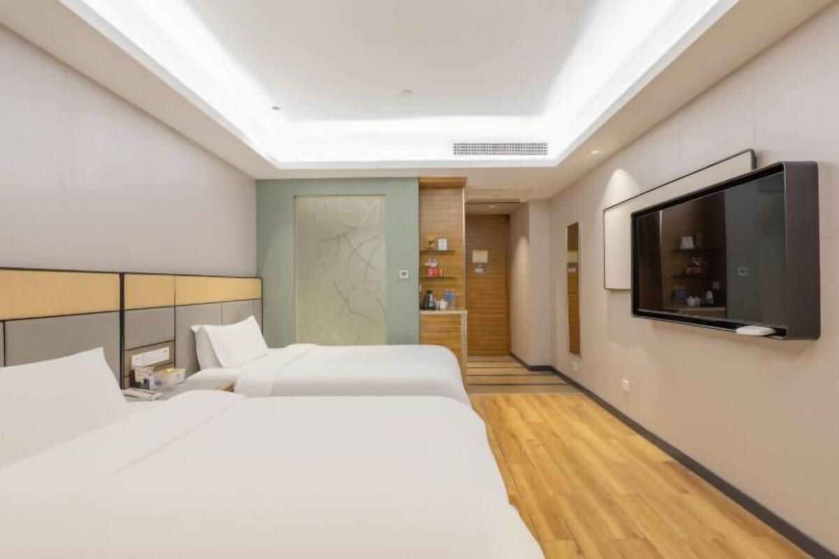 Quarto de hotel com duas camas, televisão, pequeno espaço de cozinha e claraboia.