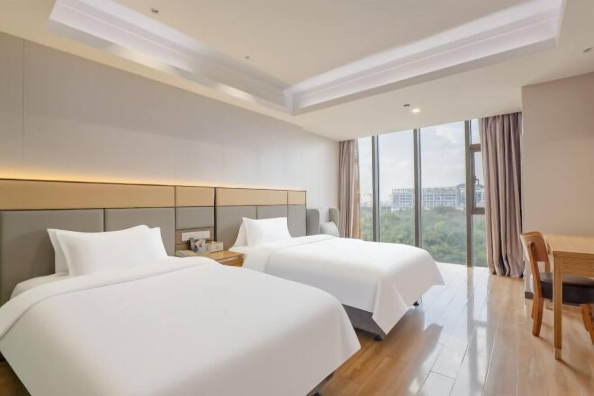 Quarto de hotel com duas camas, uma escrivaninha e uma janela grande com vista para a cidade.