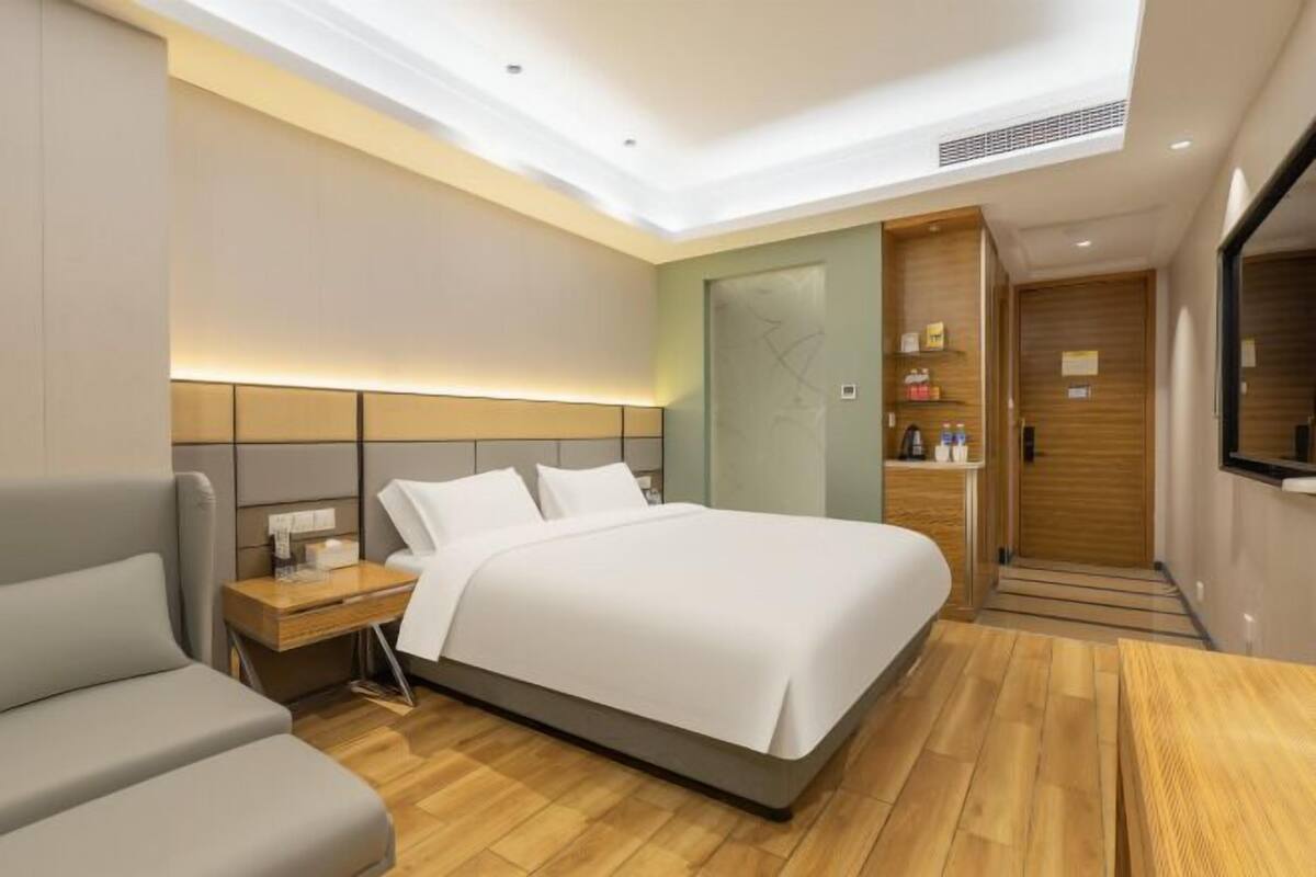 Quarto de hotel moderno com uma cama grande, uma mesinha de cabeceira, uma cadeira e um guarda-roupa.