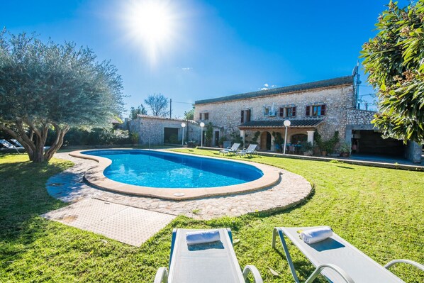 Relax by the serene pool surrounded by lush greenery and a traditional stone building in the background.