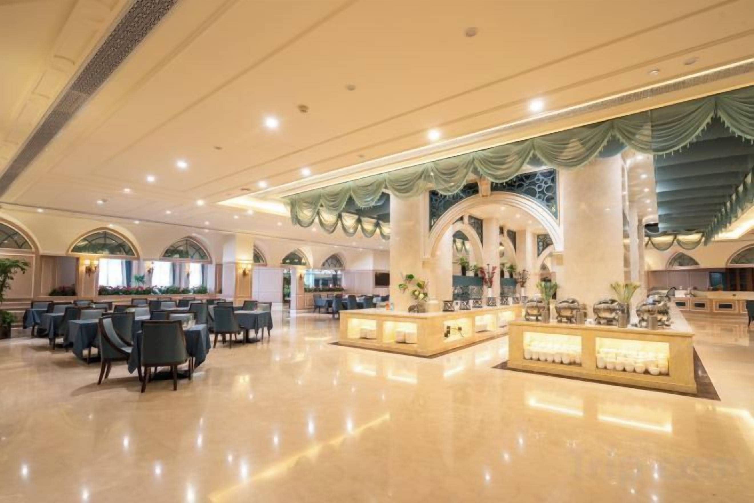 A spacious hotel lobby with a central reception desk, multiple seating areas, and a polished floor.