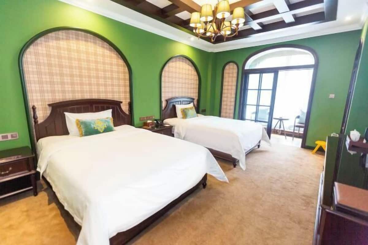 Habitació d'hotel amb dos llits, parets verdes i una finestra gran.