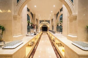 Un amplio vestíbulo de hotel con una imponente escalera de mármol, techos abovedados y un mostrador de recepción alargado.