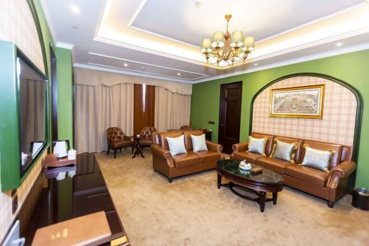A spacious living room with a brown leather sofa set, a coffee table, and a chandelier.