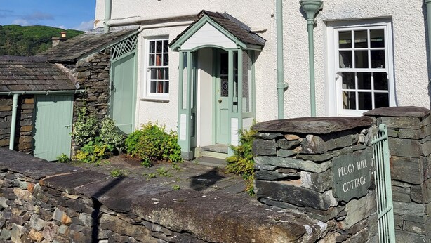 A white cottage with a stone entrance labeled "PEGGY HILL COTTAGE," a chimney, and a small porch with a door. - Peggy Hill Cottage - Two Bedroom House, Sleeps 4 (Ambleside)