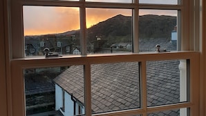 A window with a view of a village at sunset, including houses and a hill. - Peggy Hill Cottage - Two Bedroom House, Sleeps 4 (Ambleside)
