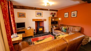 A cozy living room with a fireplace, leather sofa, and a television. - Peggy Hill Cottage - Two Bedroom House, Sleeps 4 (Ambleside)