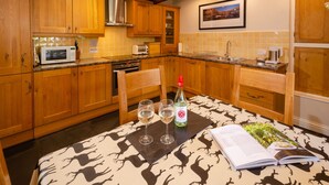 A kitchen with wooden cabinets, a microwave, a toaster, and a sink. There is a bottle of wine and glasses on the table. - Peggy Hill Cottage - Two Bedroom House, Sleeps 4 (Ambleside)