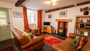 A cozy living room with leather sofas, a fireplace, a television, and a bookshelf. - Peggy Hill Cottage - Two Bedroom House, Sleeps 4 (Ambleside)