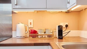Une cuisine équipée d’une bouilloire, d’une machine à café et d’un panier de fruits posé sur le plan de travail.