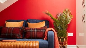 Un salon avec un canapé bleu, des coussins orange, un pouf en cuir marron et une grande plante en pot.